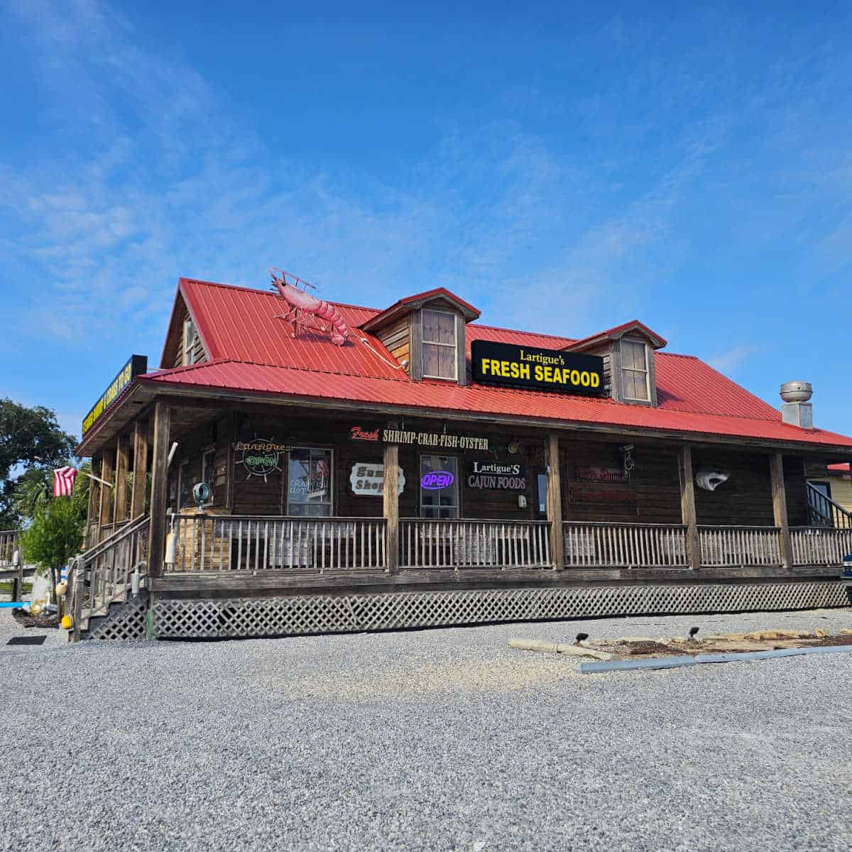 Lartigue's Fresh Seafood sign on a red roof with a large shrimp, wooden exterior with signs and a wrap around deck