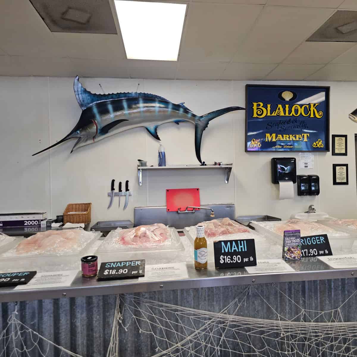 Blalock Seafood market sign on the wall next to a tune art, Trigger, mahi, snapper, and grouper filets wrapped on ice