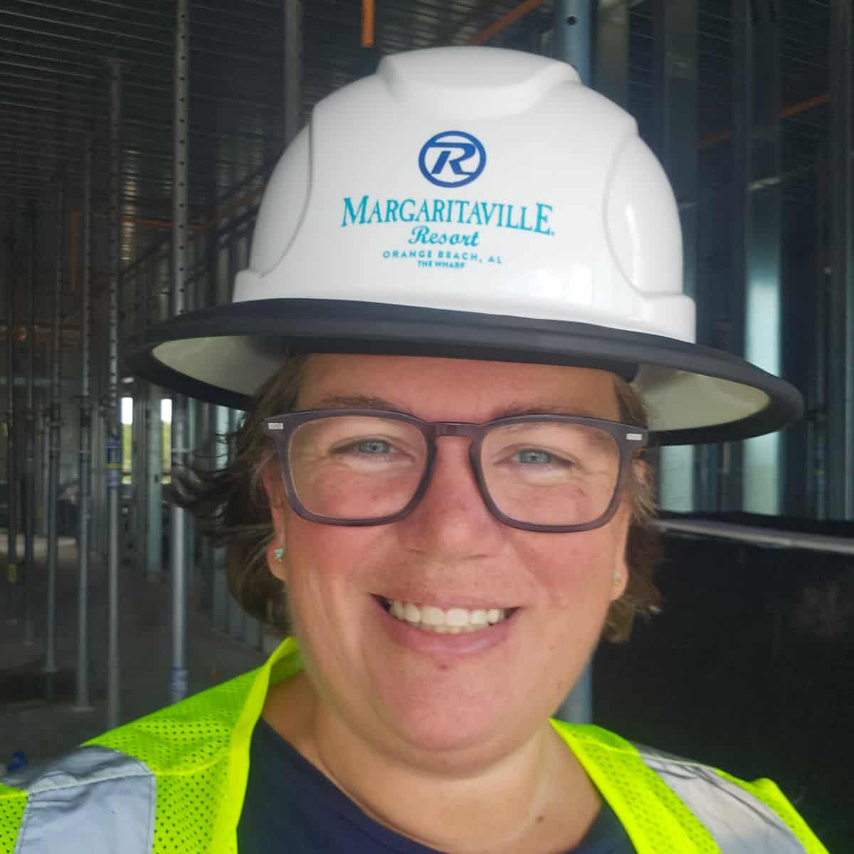 Tammilee wearing a Margaritaville Resort Orange Beach Hard Hat and safety vest with construction behind her