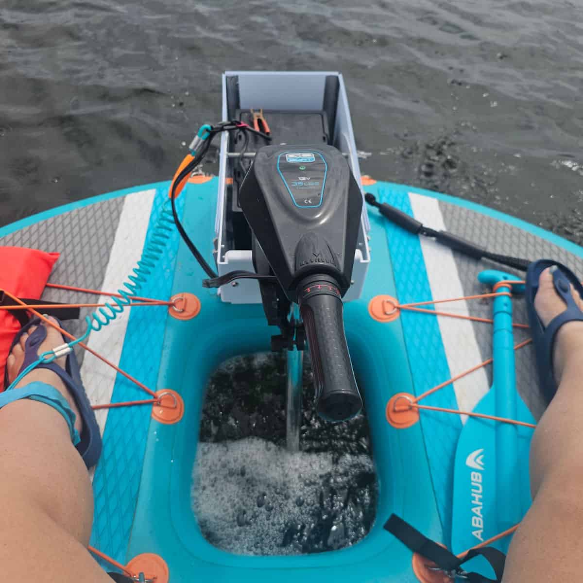 looking down at legs on either side of a circle boat with a motor in the middle, paddle held to the boat
