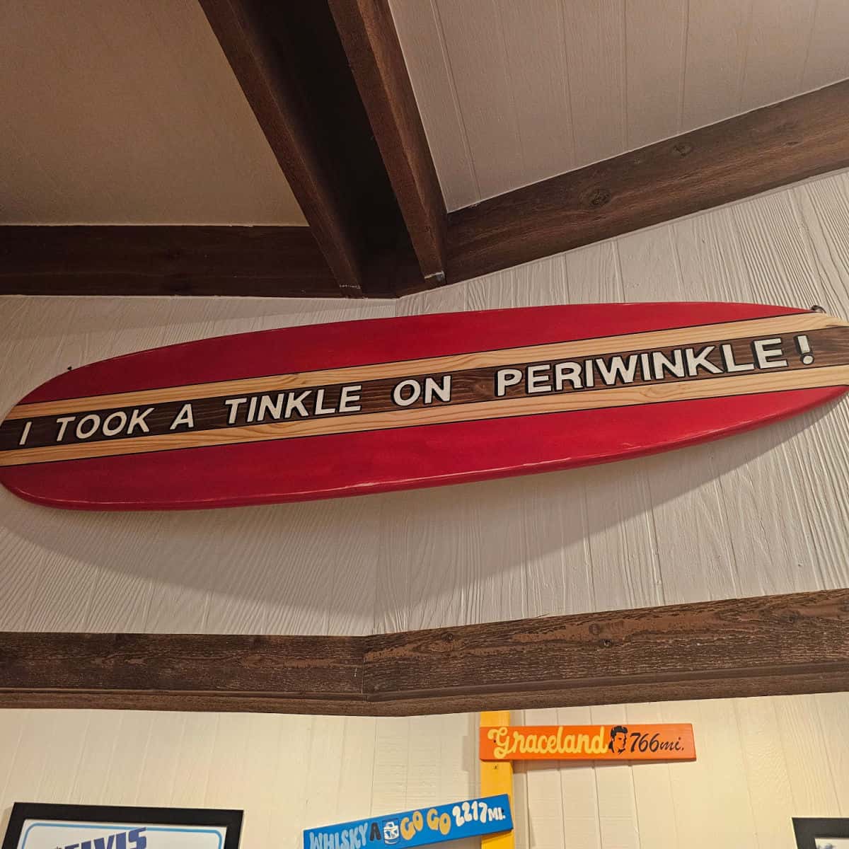 Red and brown surfboard with "I took a tinkle on periwinkle" printed down the middle