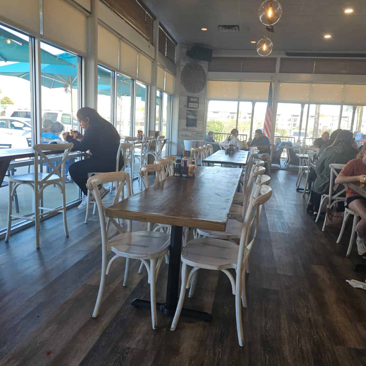 indoor seating with rows of long tables with white chairs, long counter along the windows with tall stools, people eating at the tables