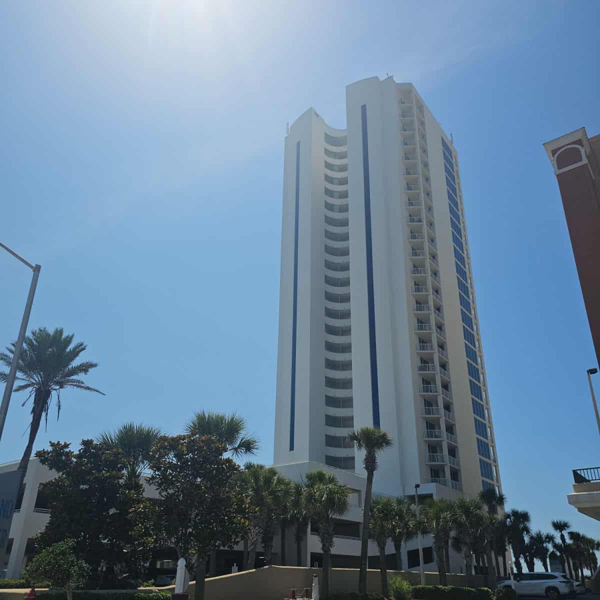 Tall Island Tower condo building with glass windows down the side, palm trees around the base
