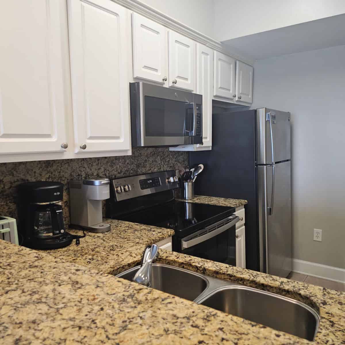 kitchen with stainless steel appliances, white upper cabinets, and brown granite counters