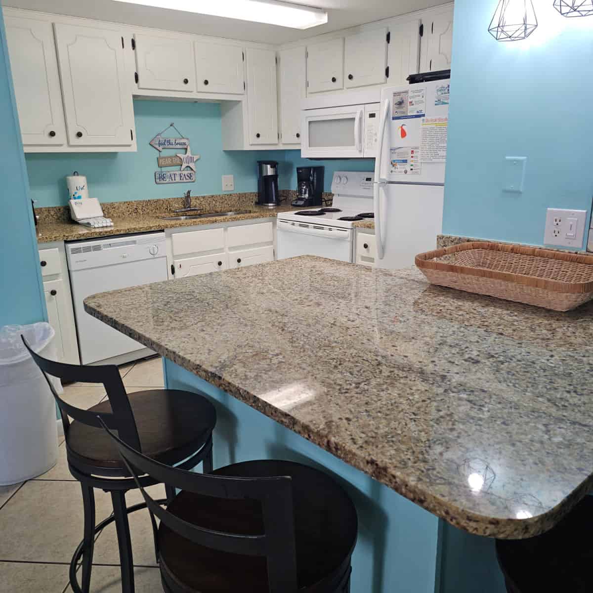 Kitchen with blue walls, counter with two tall stools, white cabinets and white appliances