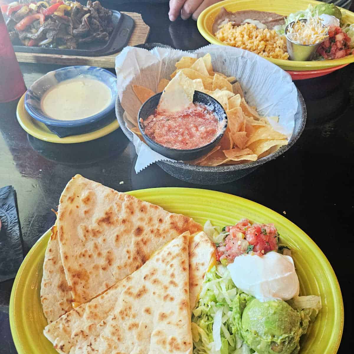 table with a quesadilla plate, chips and salsa, fajitas, plate with rice, beans, and toppings plus queso