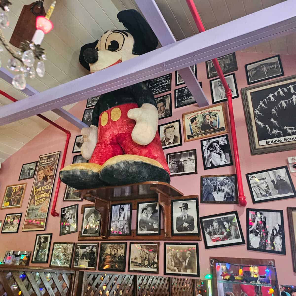 mickey mouse hanging from the ceiling in front of a pink wall covered in black and white photos
