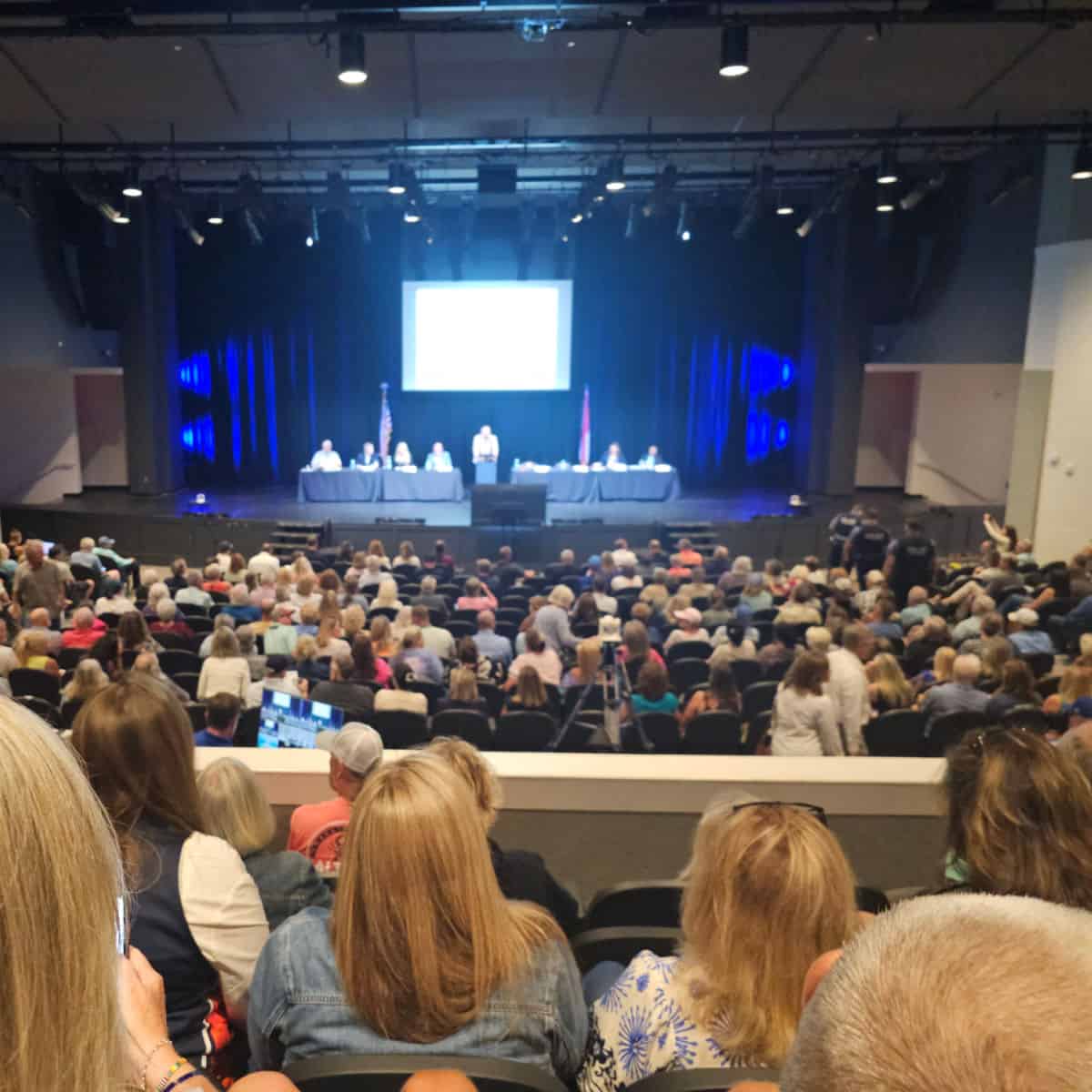 Looking down from an elevated seat to the city council on stage with a screen behind them.