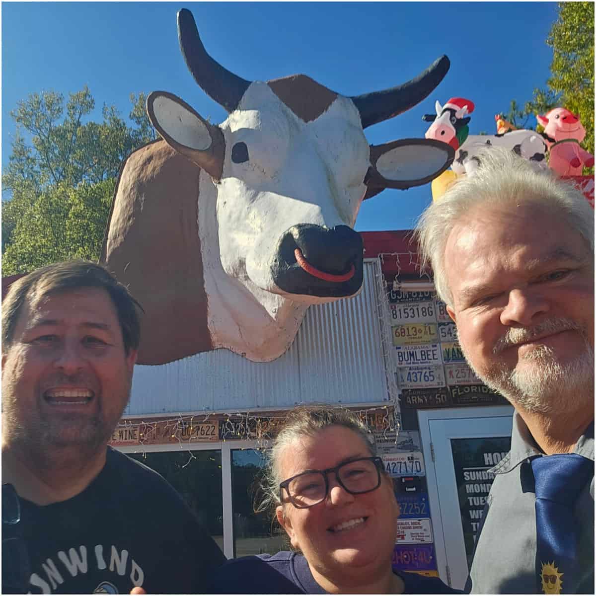Tammilee and John with Bama Bob, with a large cow head coming out of the building behind them.