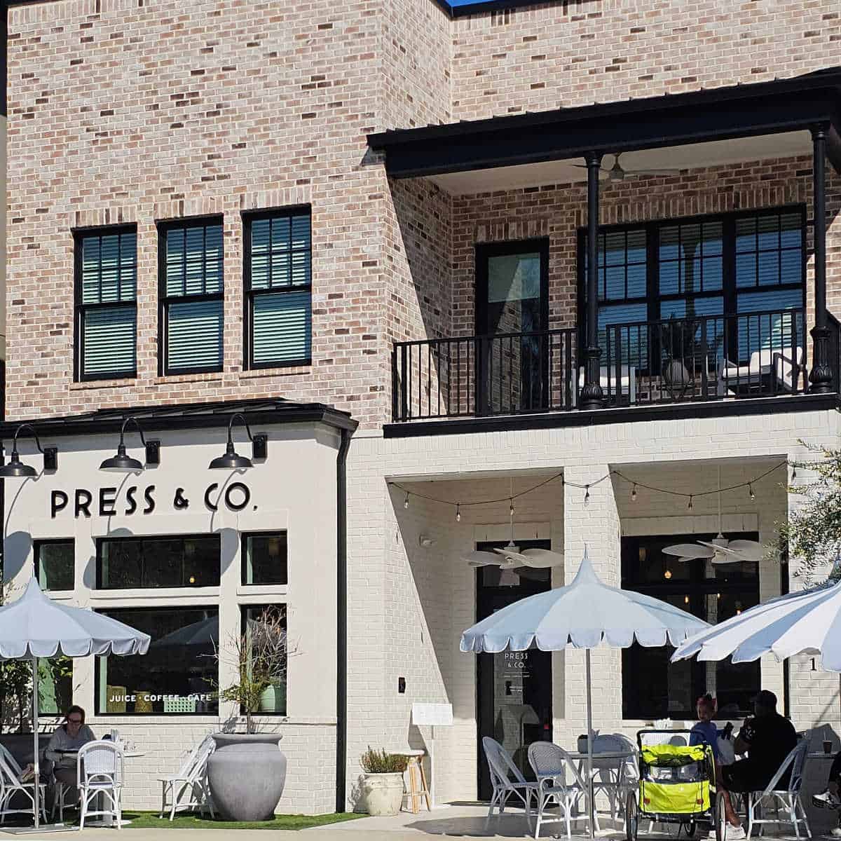 Press & Co exterior with white umbrellas and chairs outside, brick building above the coffee shop