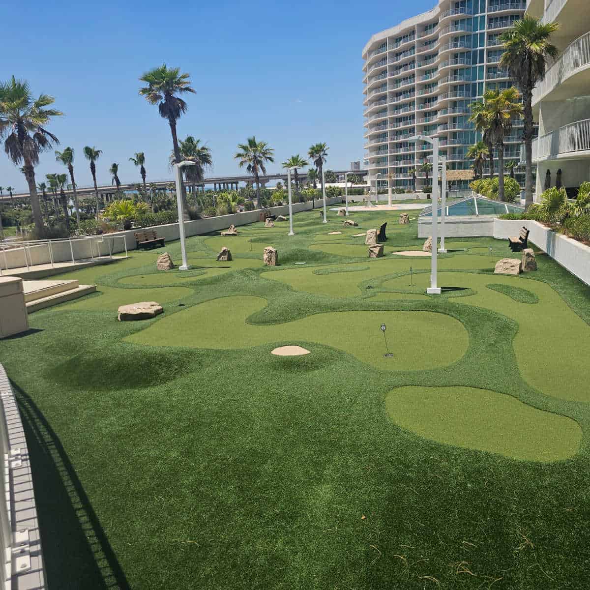 mini golf course on the top of a building with palm trees in the background, buidlings on the left side