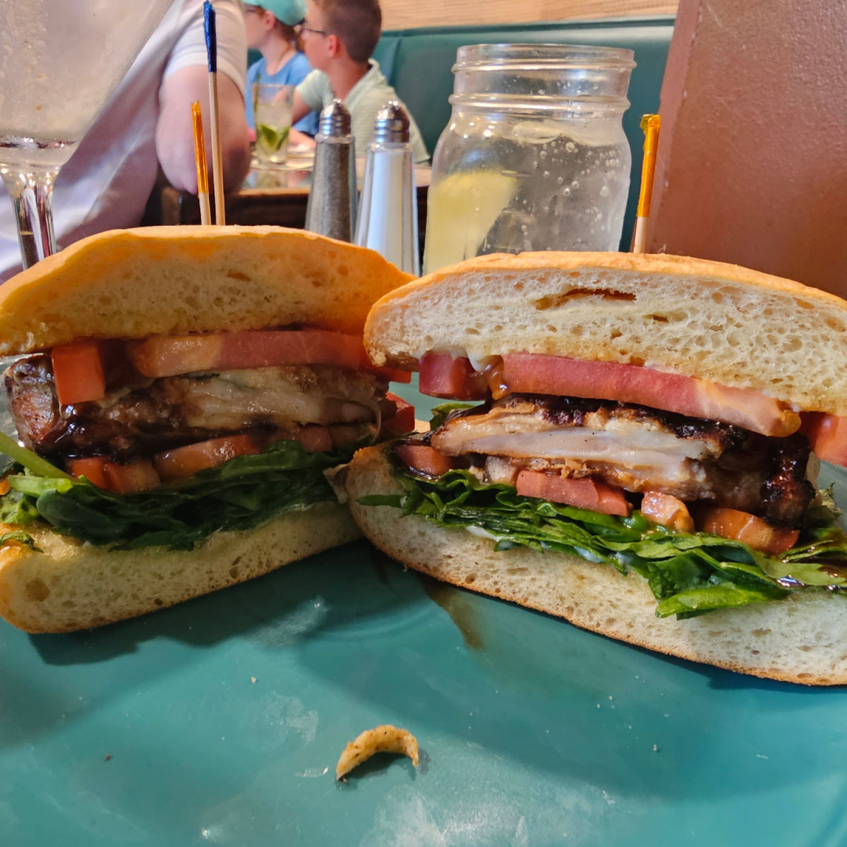 chicken sandwich with lettuce and tomato on focaccia, glass of water behind it