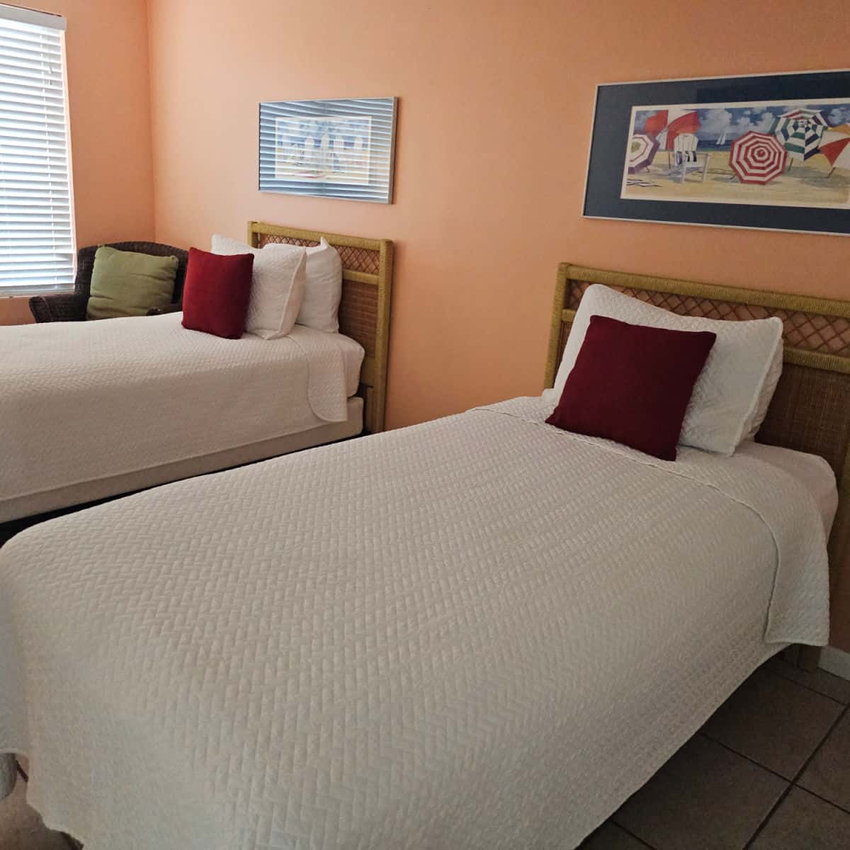 Two beds with white linens and a red pillow, art prints over beach scenes over the beds