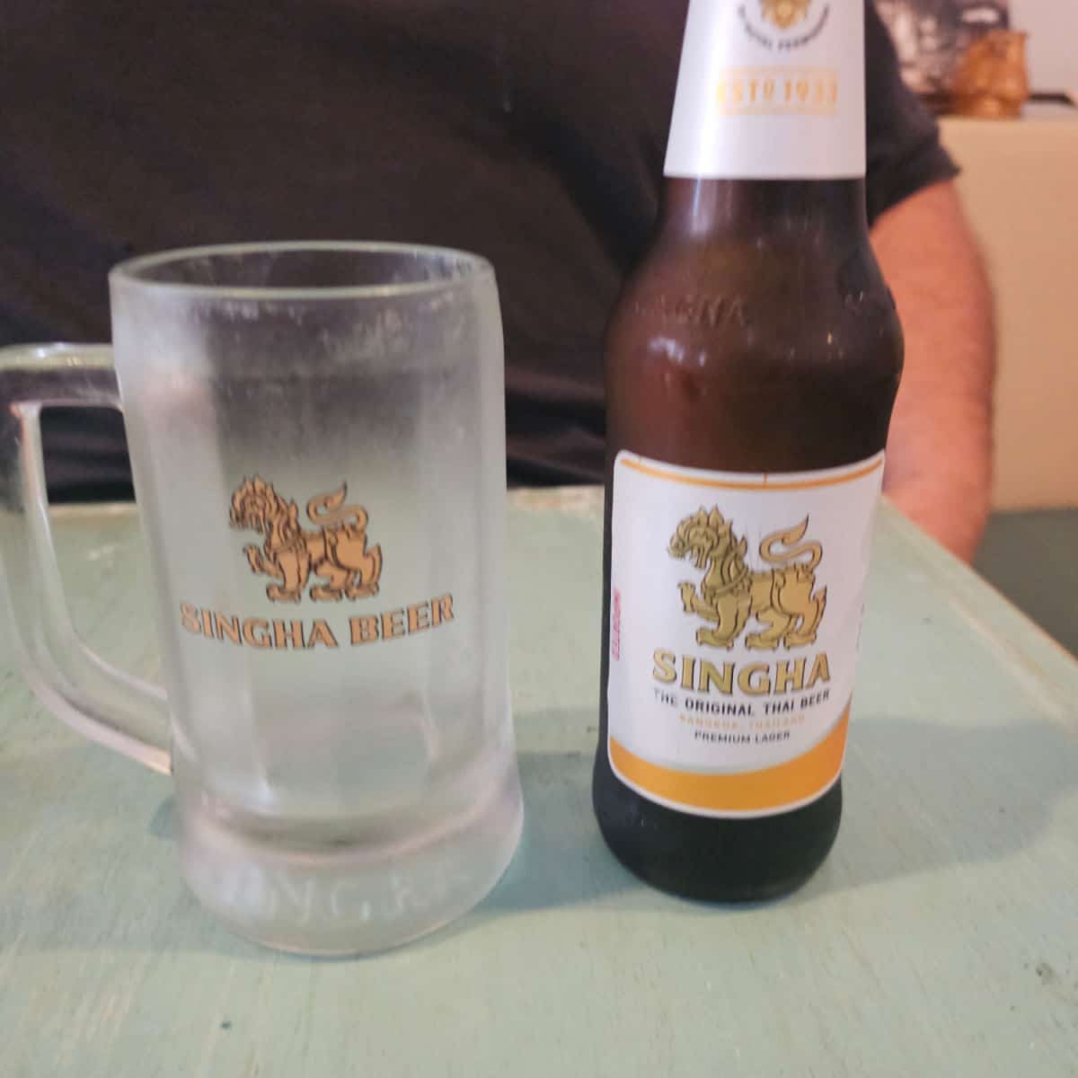Singha beer bottle next to a Singha Beer glass on a table