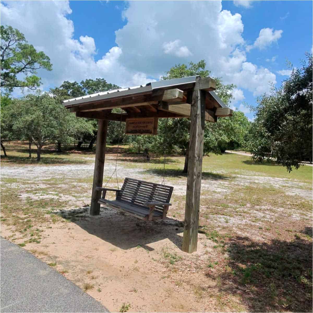 Swinging bench with a wooden cover with trees and trail next to it