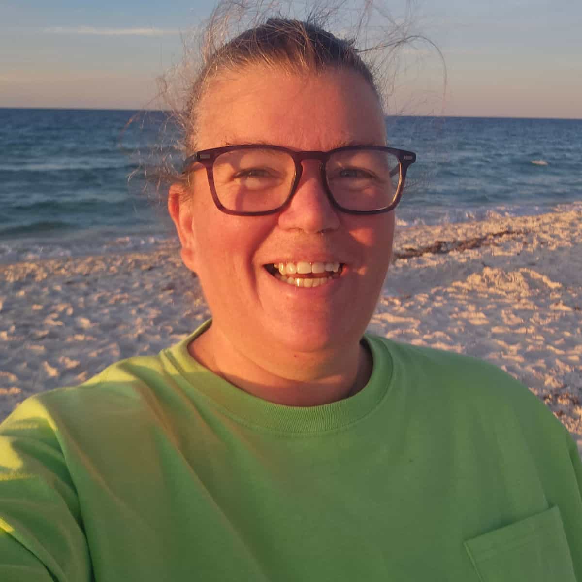 Tammilee smiling on the beach in a green shirt