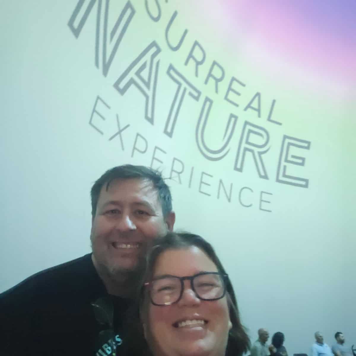 Tammilee and John standing in front of a huge screen with Surreal Nature Experience printed on it