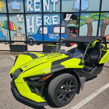 neon green Slingshot in front of a rent here Gulf Coast Rental Co painted window