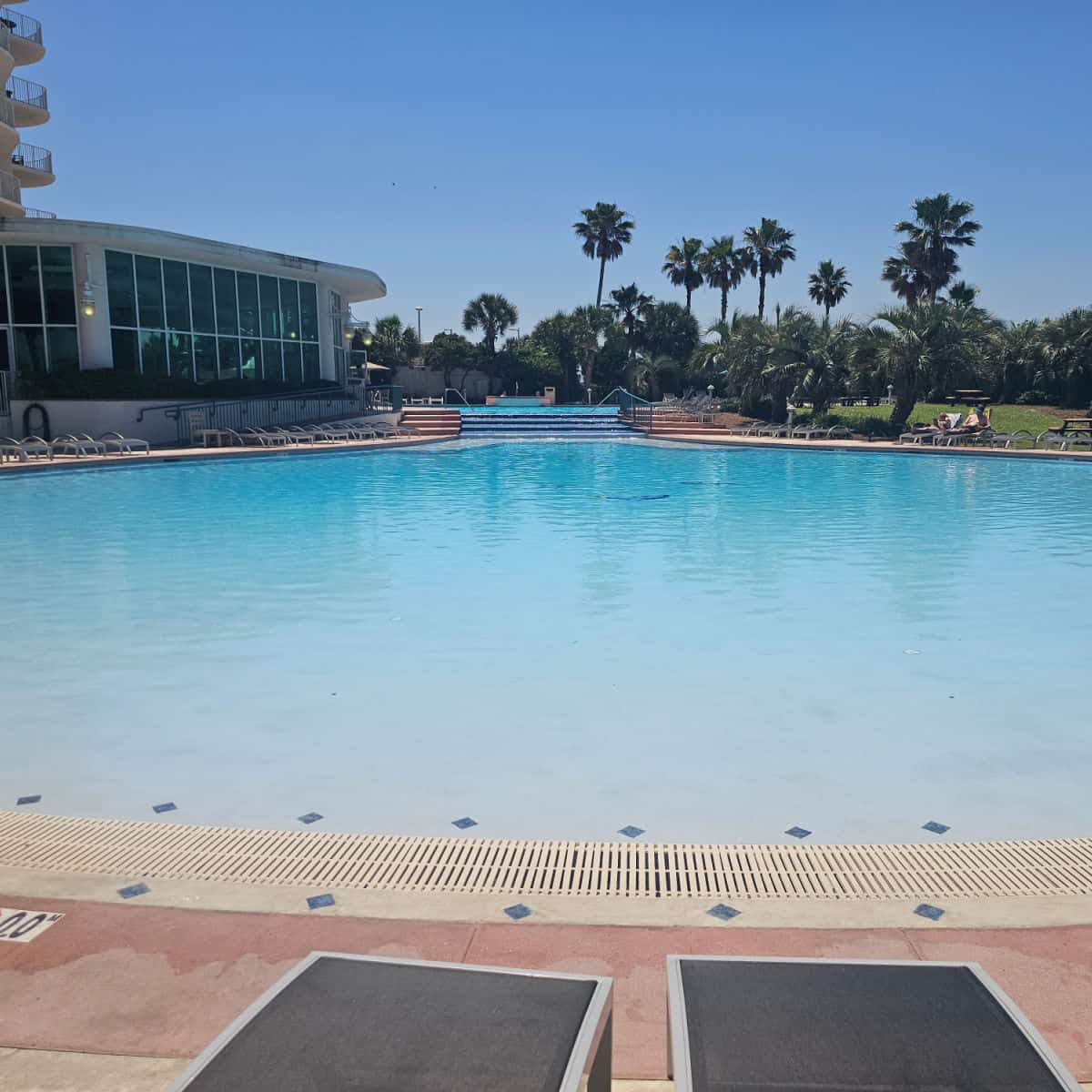 large zero entry pool with palm trees in the background condo buiding in the left corner