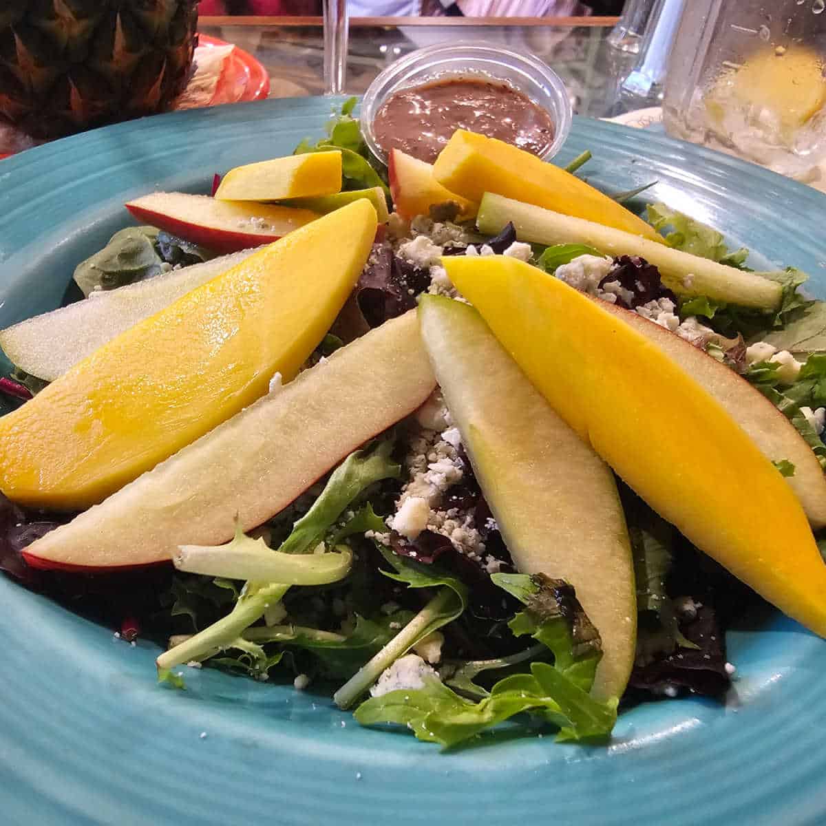 salad with mango and apple slices on top, dressing in a cup