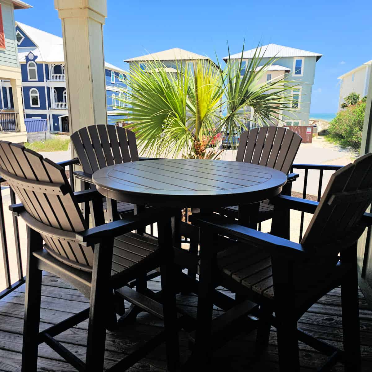 balcony with a round table and tall Adirondack chairs, vacation houses and Gulf waters in the background