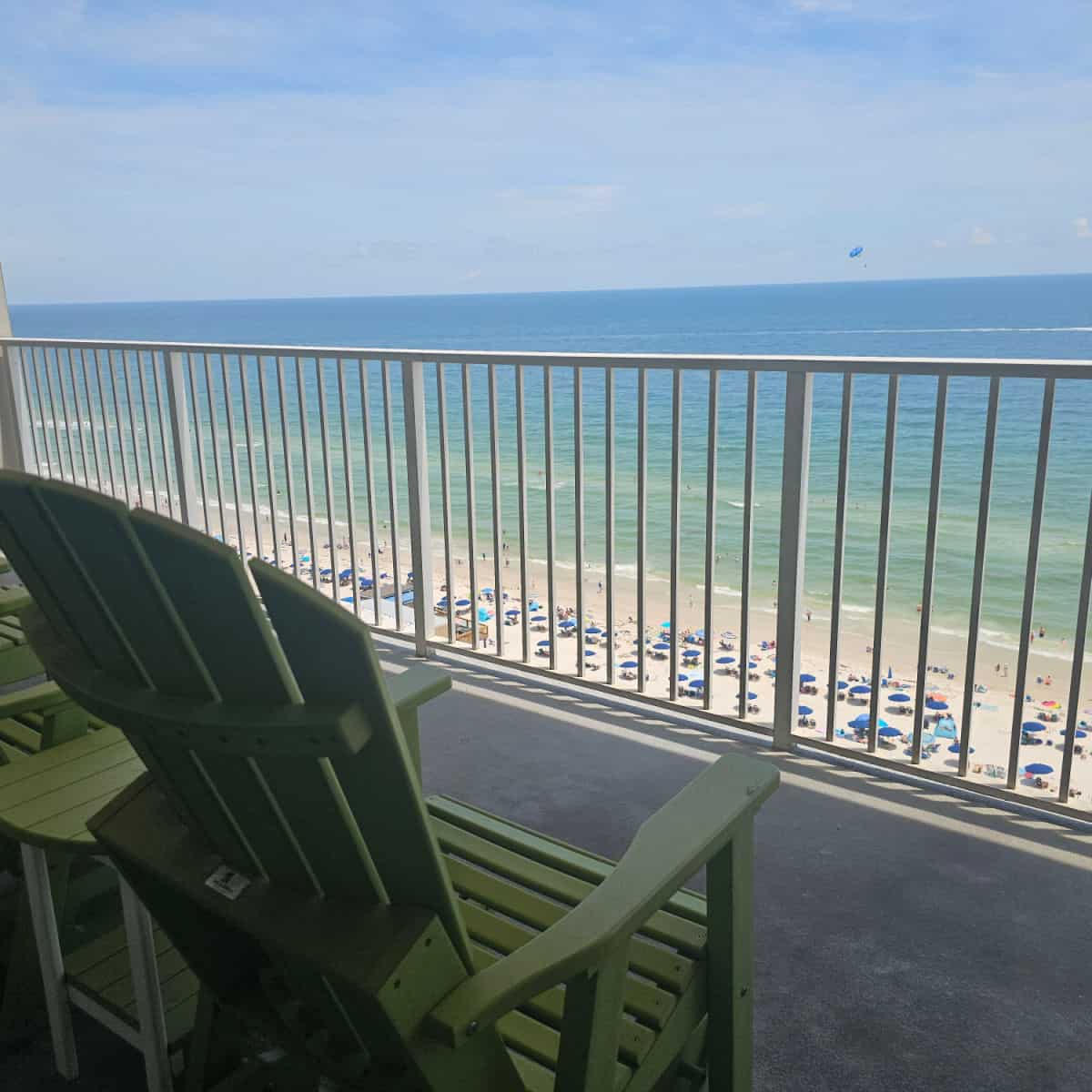 balcony views of the Gulf with a parasailing boat and umbrella on the water, green adirondack chairs