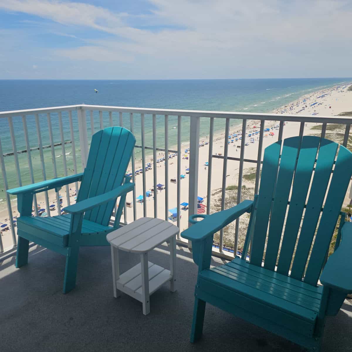 balcony with two blue adirondack chairs and a white table looking out over the Gulf and Gulf Shores beach