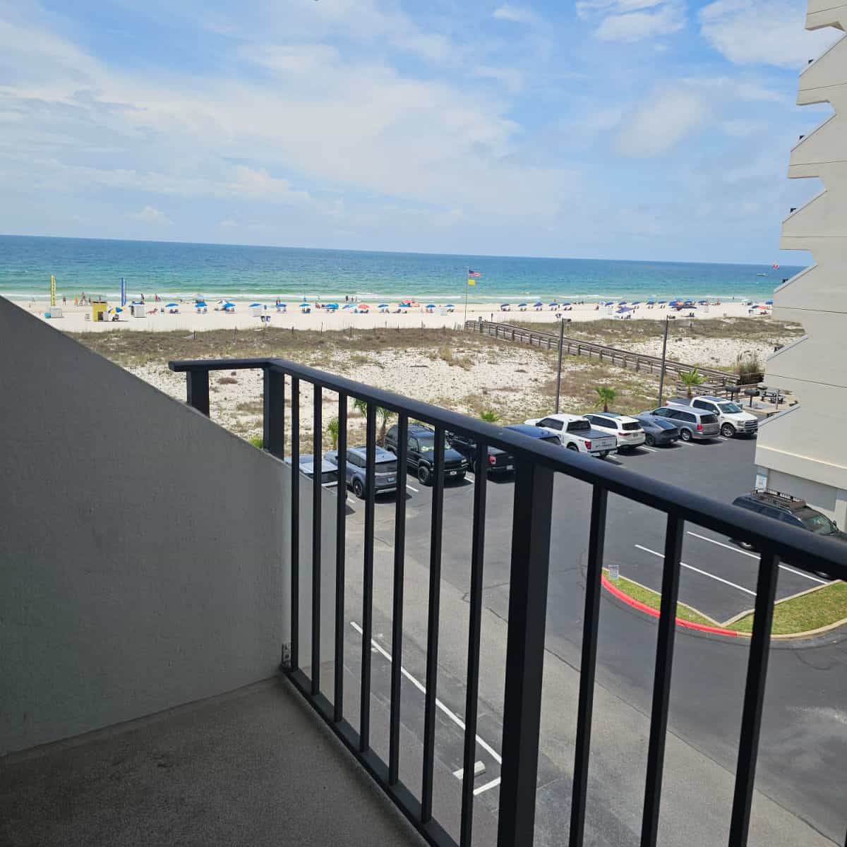 Balcony with dark rail, looking over the parking lot to white sand beach and gorgeous Gulf waters