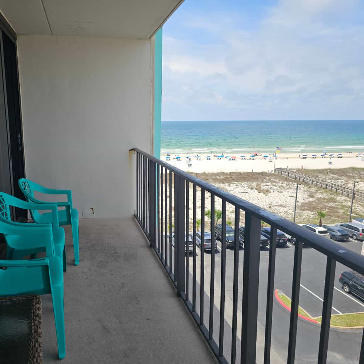Balcony with turquoise plastic chairs, views over the balcony to the Gulf and white sand, parking lot below