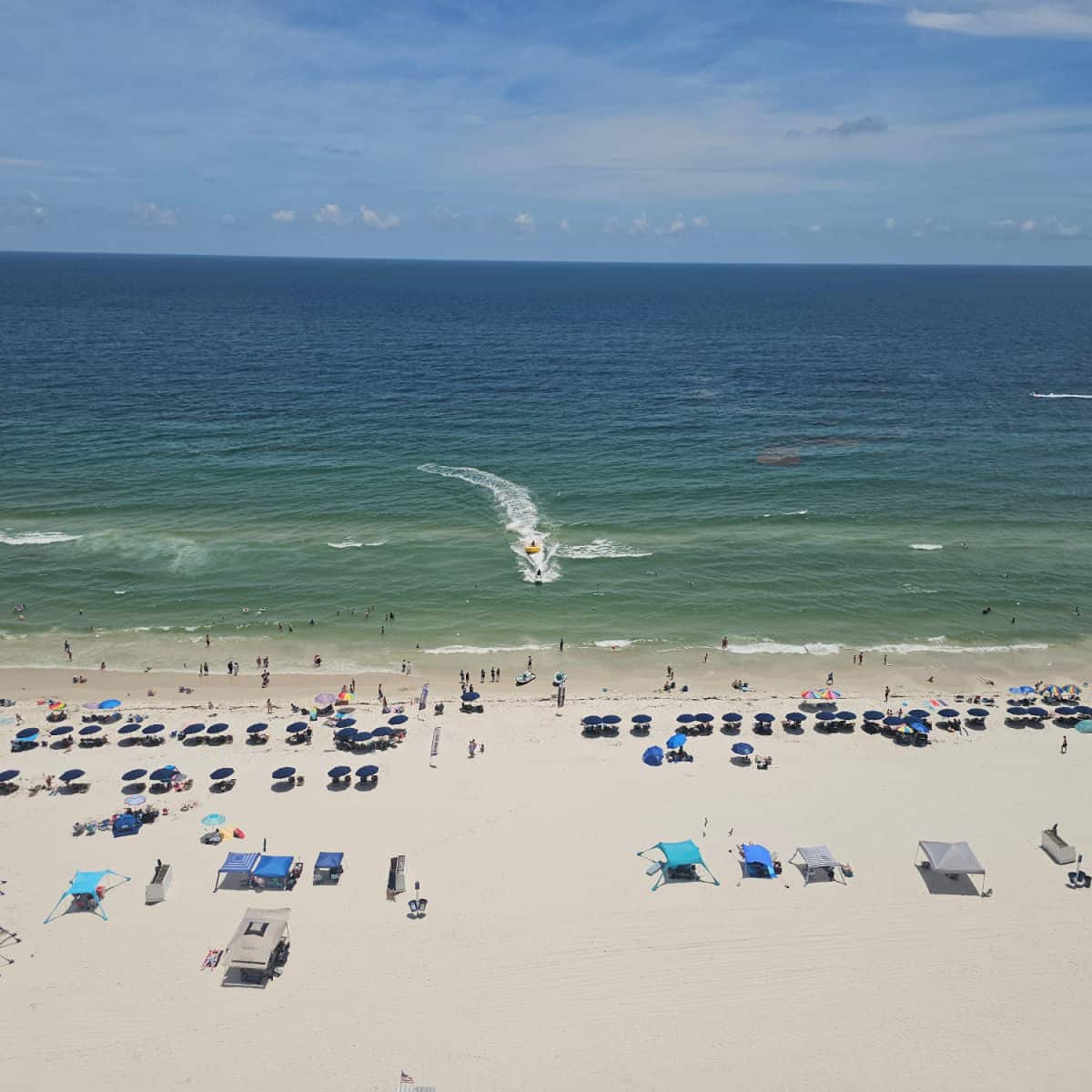 looking down to the beach with umbrellas and tents lined on the beach, banana boat pulling back up to the shore