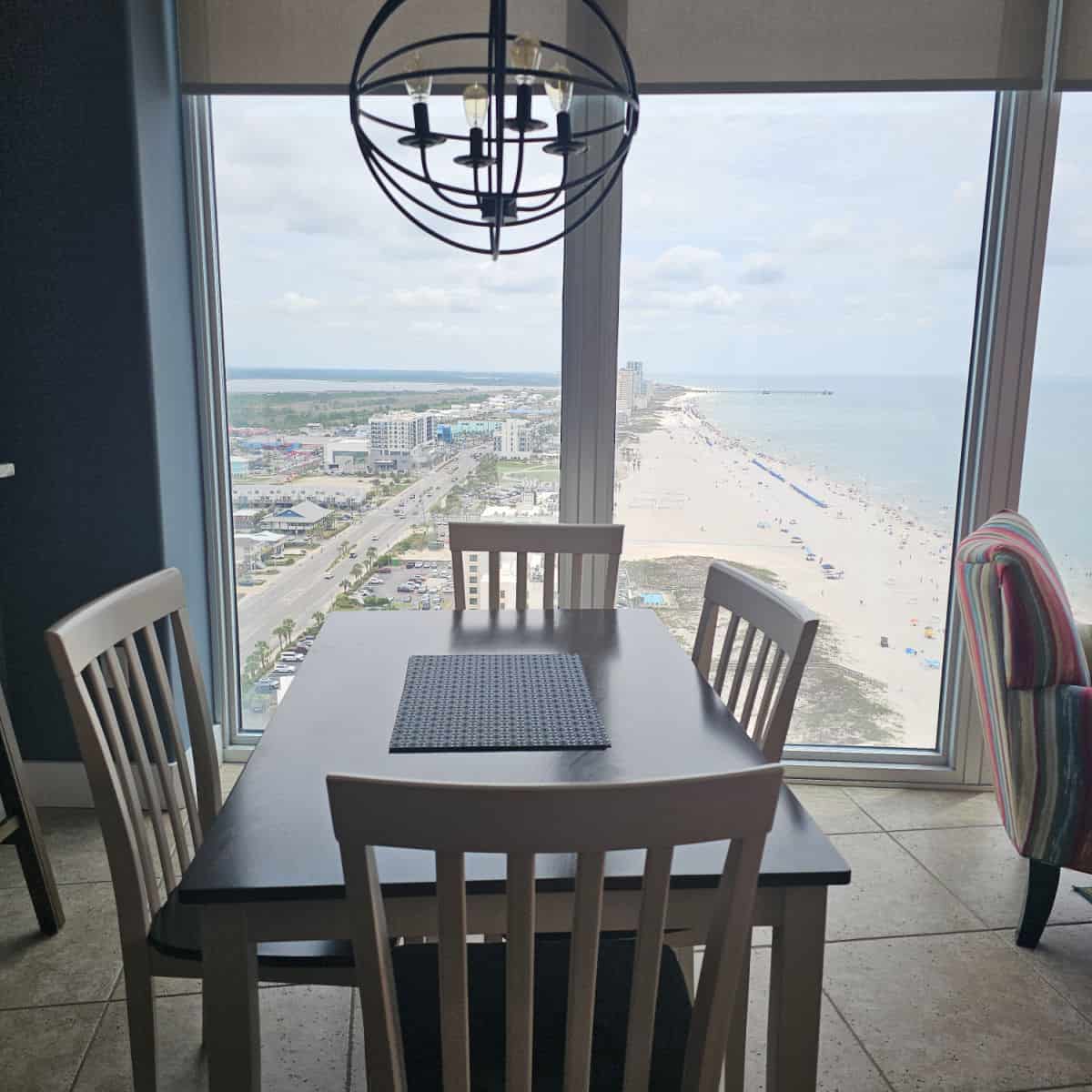 Table and chairs under a black metal lamp, picture windows looking down Gulf Shores beach with the pier in the distance