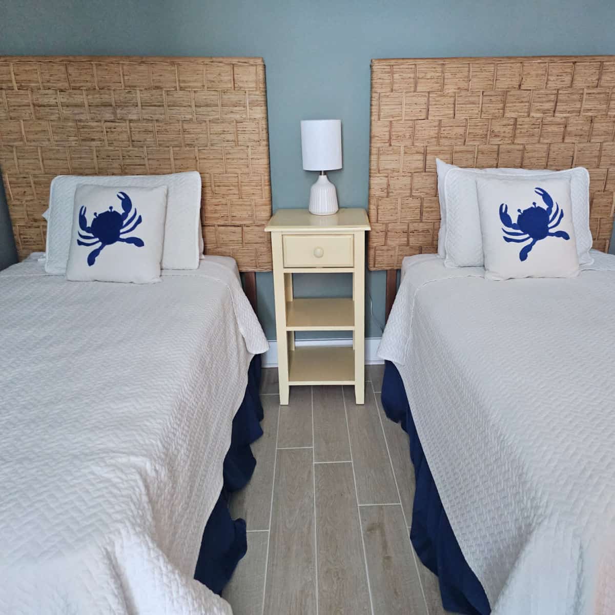 Bedroom with two twin beds, white linens on the beds with crab pillows, yellow small nightstand between the beds with a white lamp