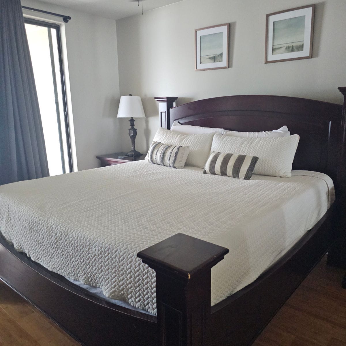 bedroom with wooden bed frame, two art prints on the wall above the bed, curtains in the corner with a portion of sliding glass door
