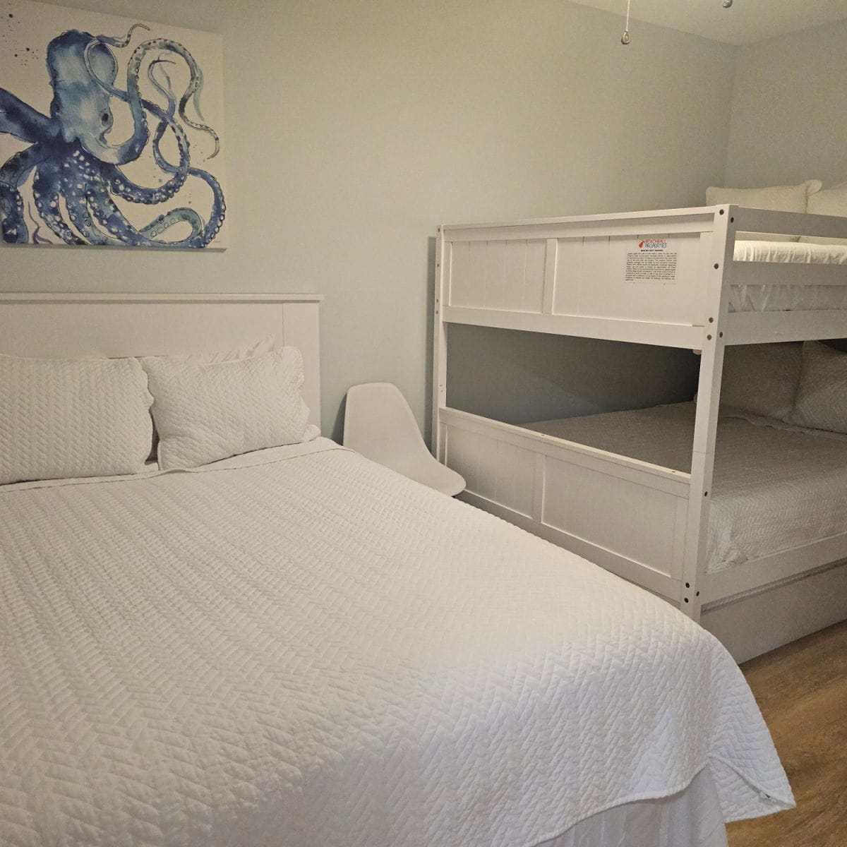 Bedroom with bed with white linens, bunkbeds in the corner, octopus art on the wall.