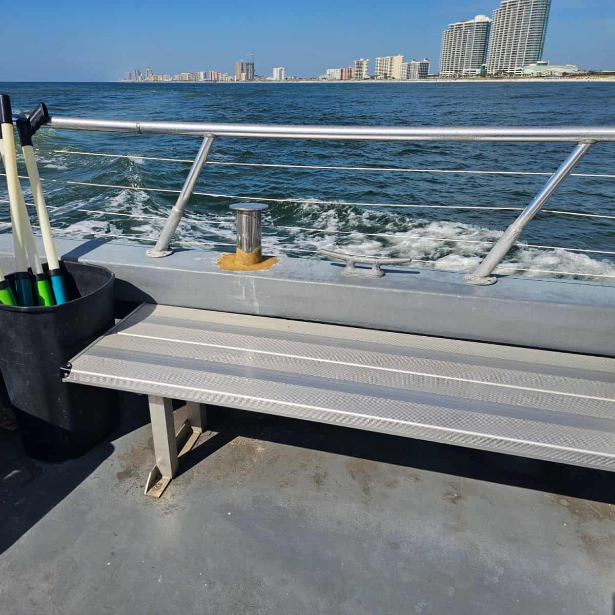 bench seating on the side of a boat with a garbage can with water guns, large condos along the beach