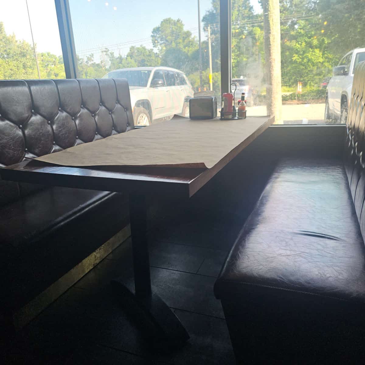 booth with leather bench and table covered in paper, cars outside in the parking lot