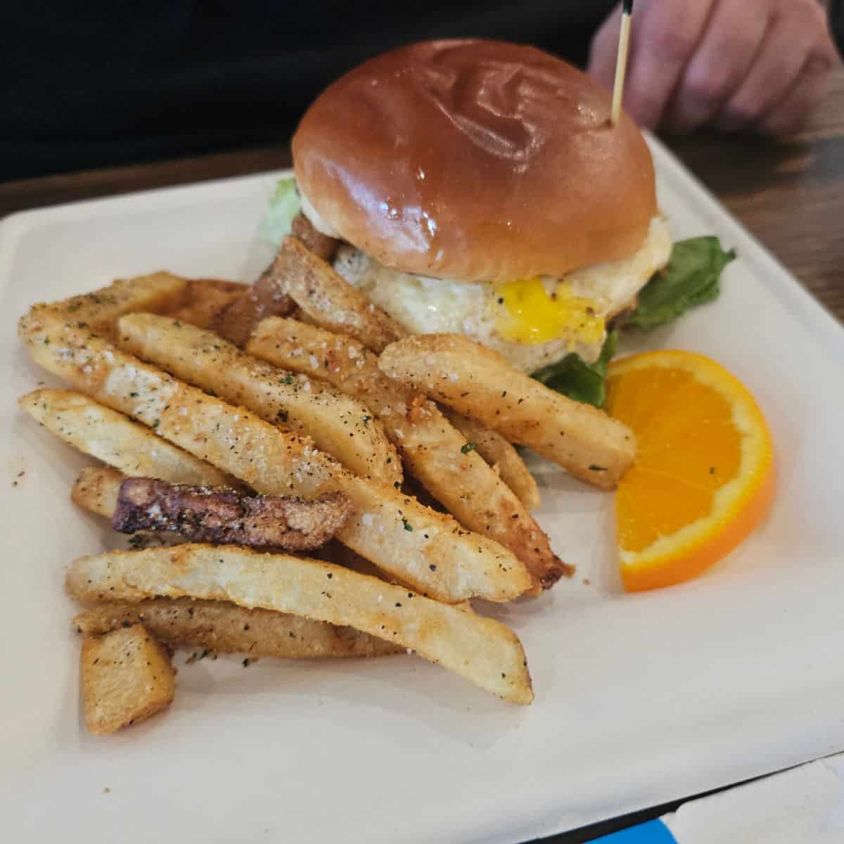 white plate with seasoned fries, an orange wheel half, and a breakfast burger