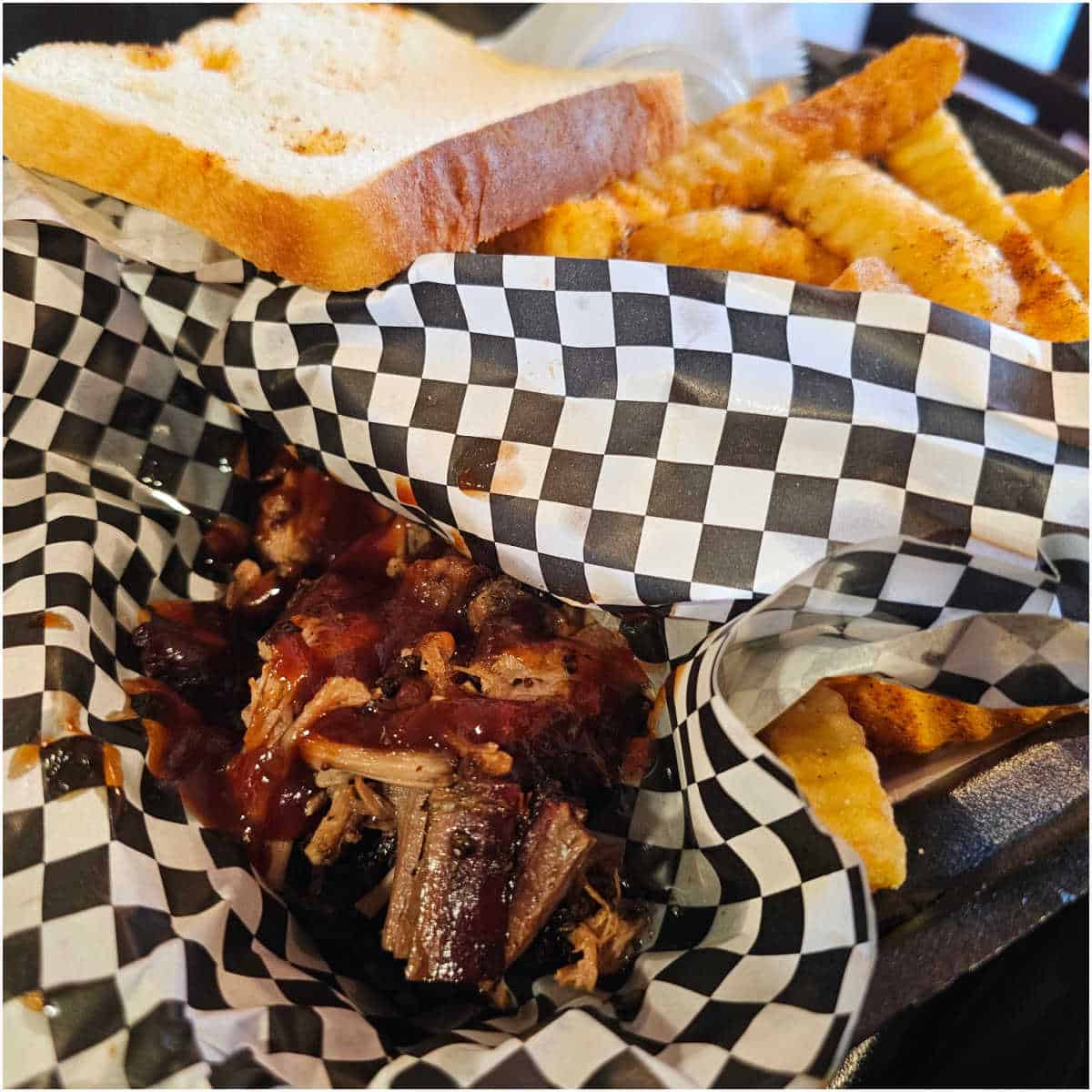 container with checkered paper with brisket, fries, and a slice of bread