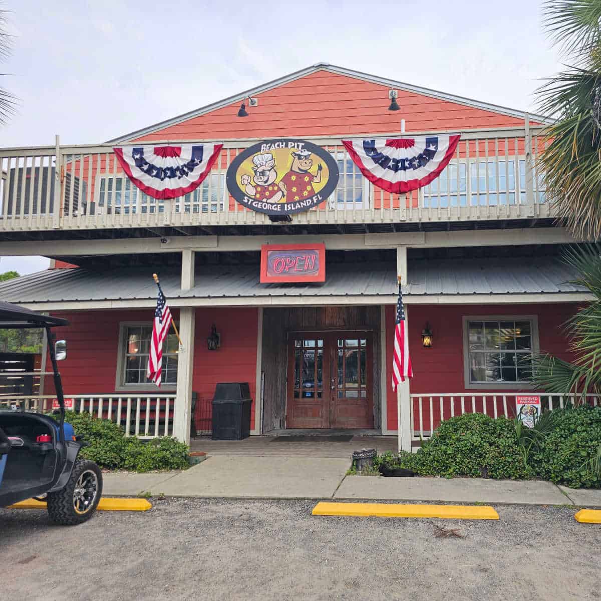Beach Pit St George Island Fl sign with a cartoon pig and cow on the front of a restaurant with orange red paint, covered entrance to the restaurant with two brown doors