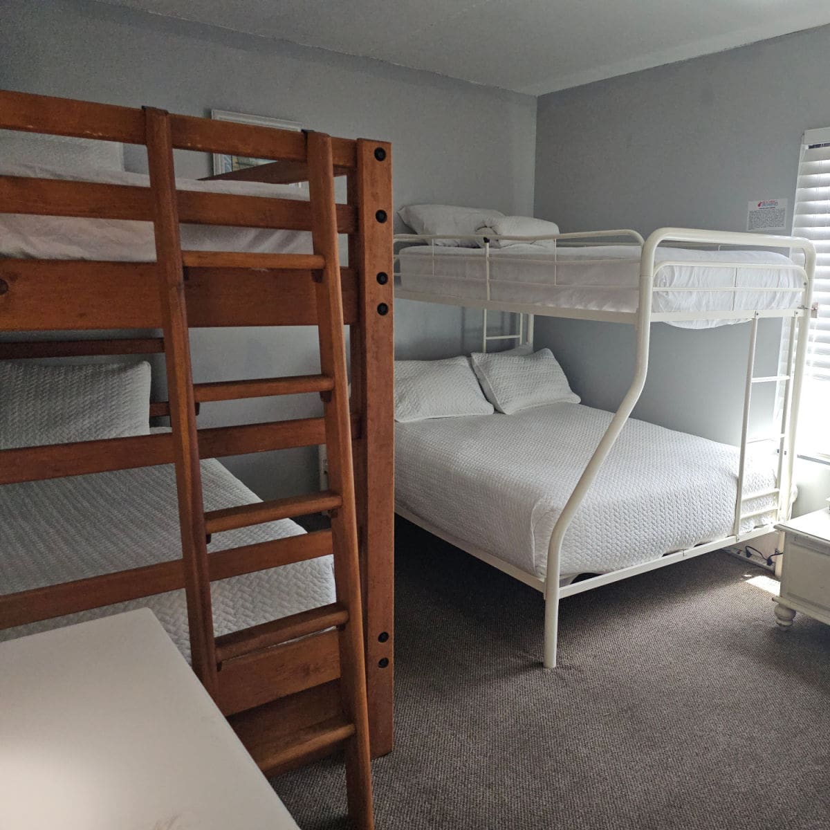 Bedroom with bunkbeds, one wooden bunkbed and one white metal bunkbed all with white linens