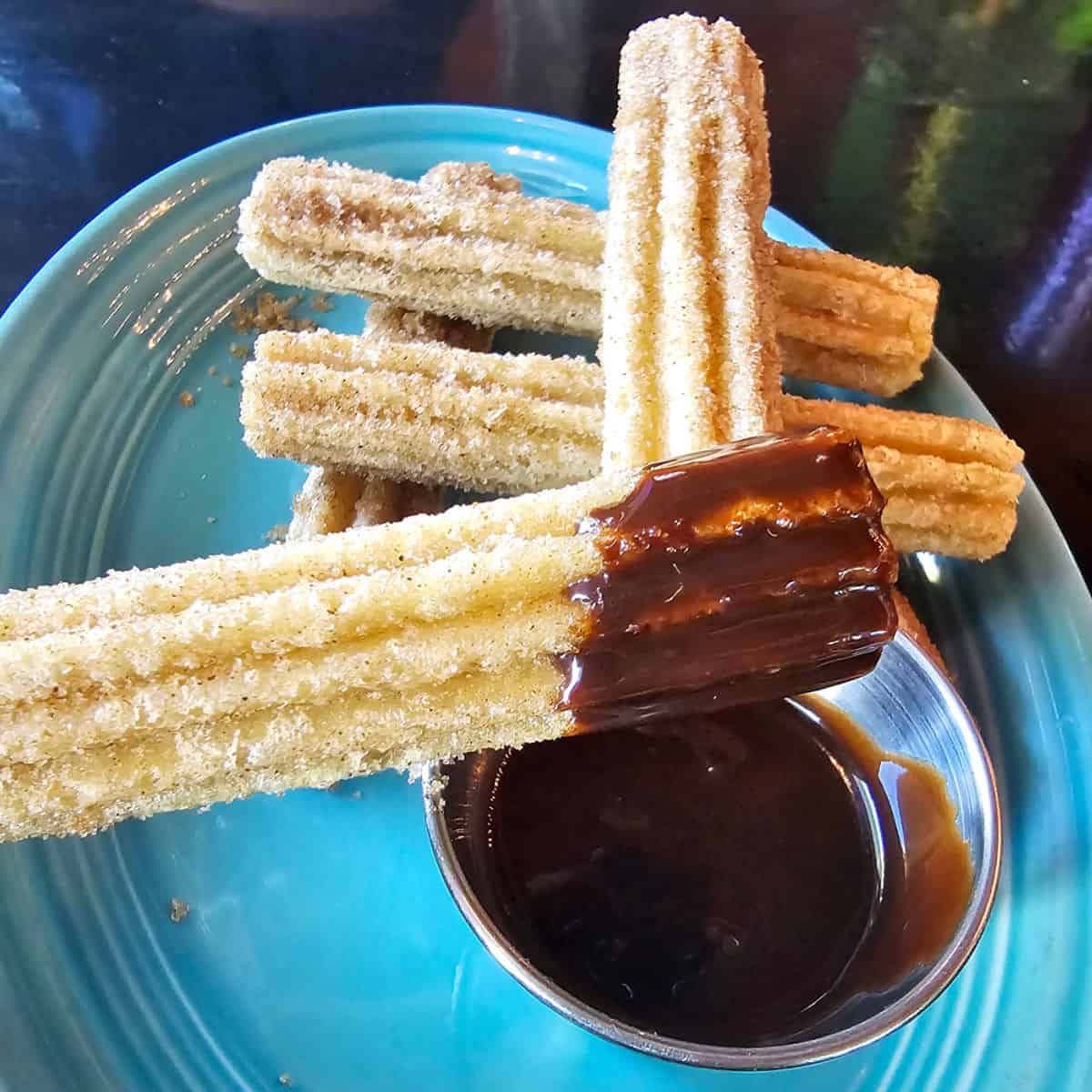 churros on a blue plate with the top one dipped in chocolate