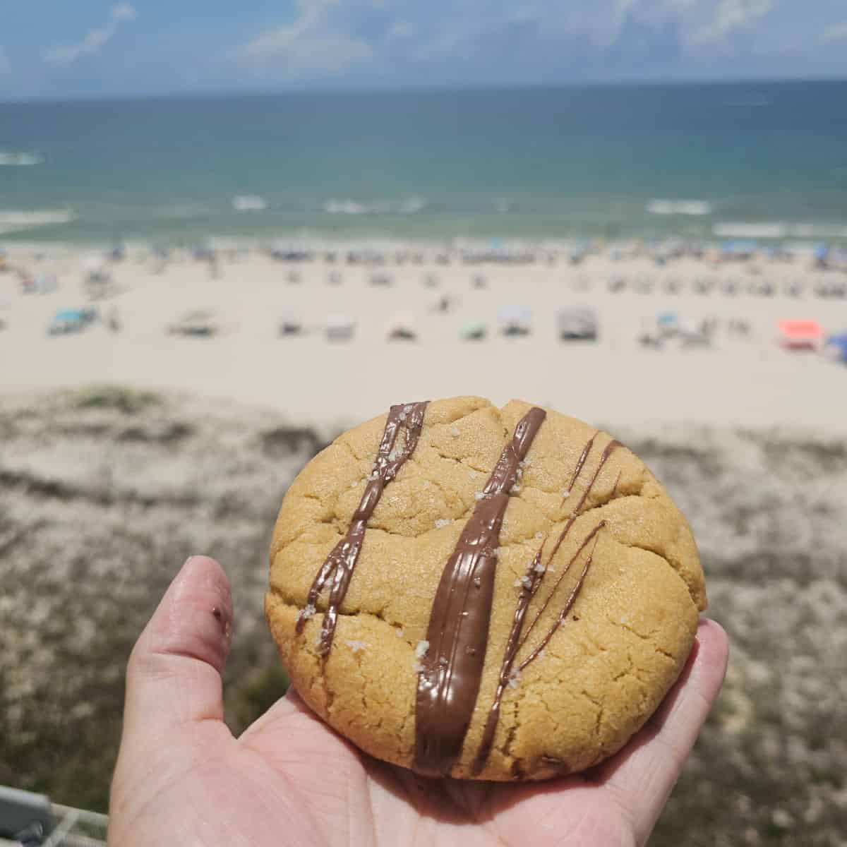 hand holding a crumbl cookie with the beach in the background
