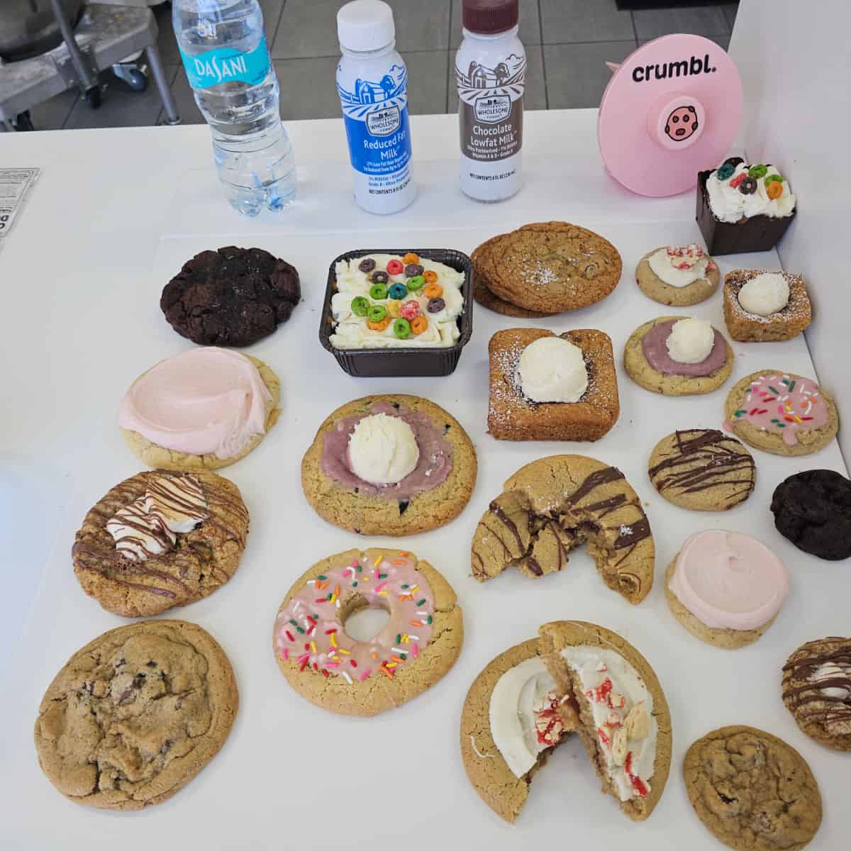 assortment of Crumbl cookies on a white counter with milk containers behind them