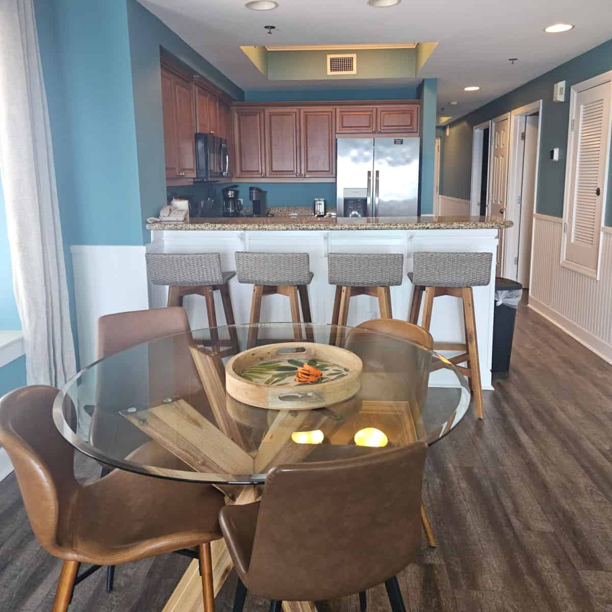 kitchen and dining room area with a glass table with leather chairs, tall stools at the counter, kitchen and hallway