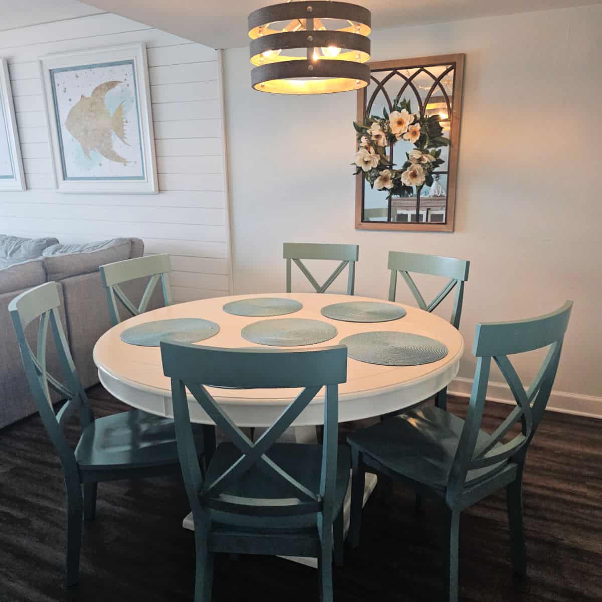 circle dining room table with placemats with turquoise chairs, chandelier over the table, fish art on the wall