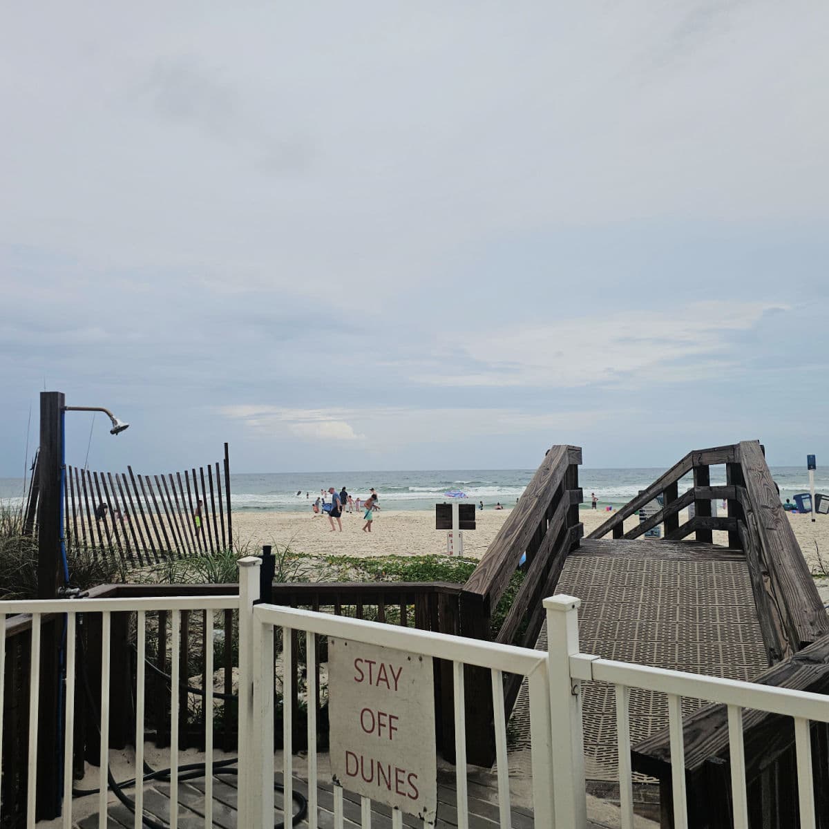 gate leading to a raised boardwalk over the sand dunes and an outdoor shower , gulf waters and beach in the background