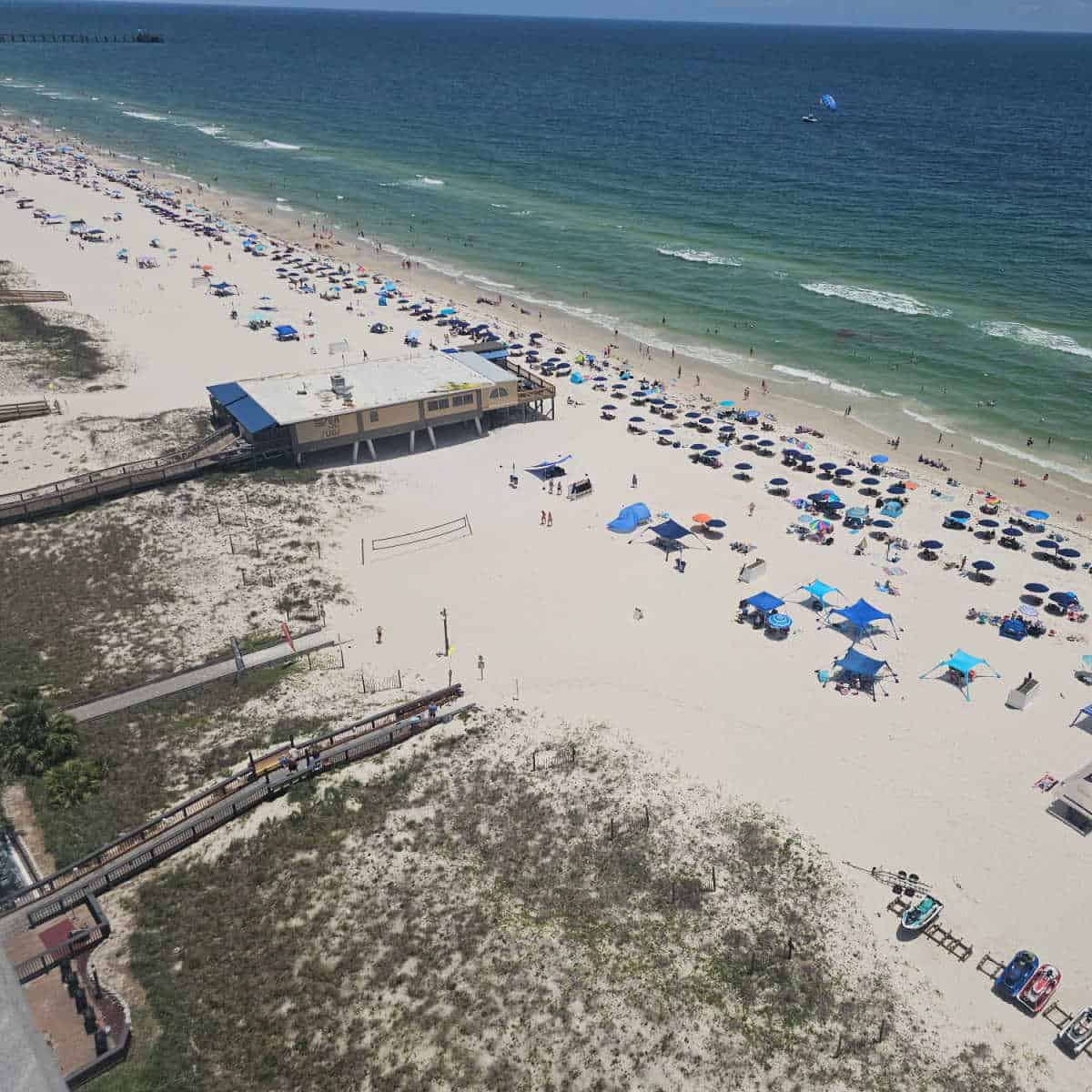 looking down to the beach from a higher elevation, boardwak over the sand dunes, beach umbrellas lining the beach, Sea n Suds restaurant