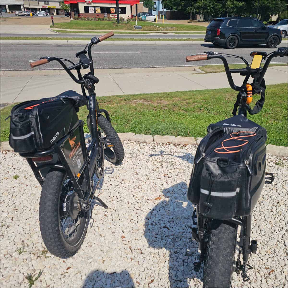 two e-bikes from Amberjack on a gravel pad with cars on the road in front of the gravel