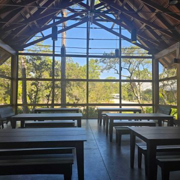 inside a building with an a-frame roof, large windows, and tables and benches