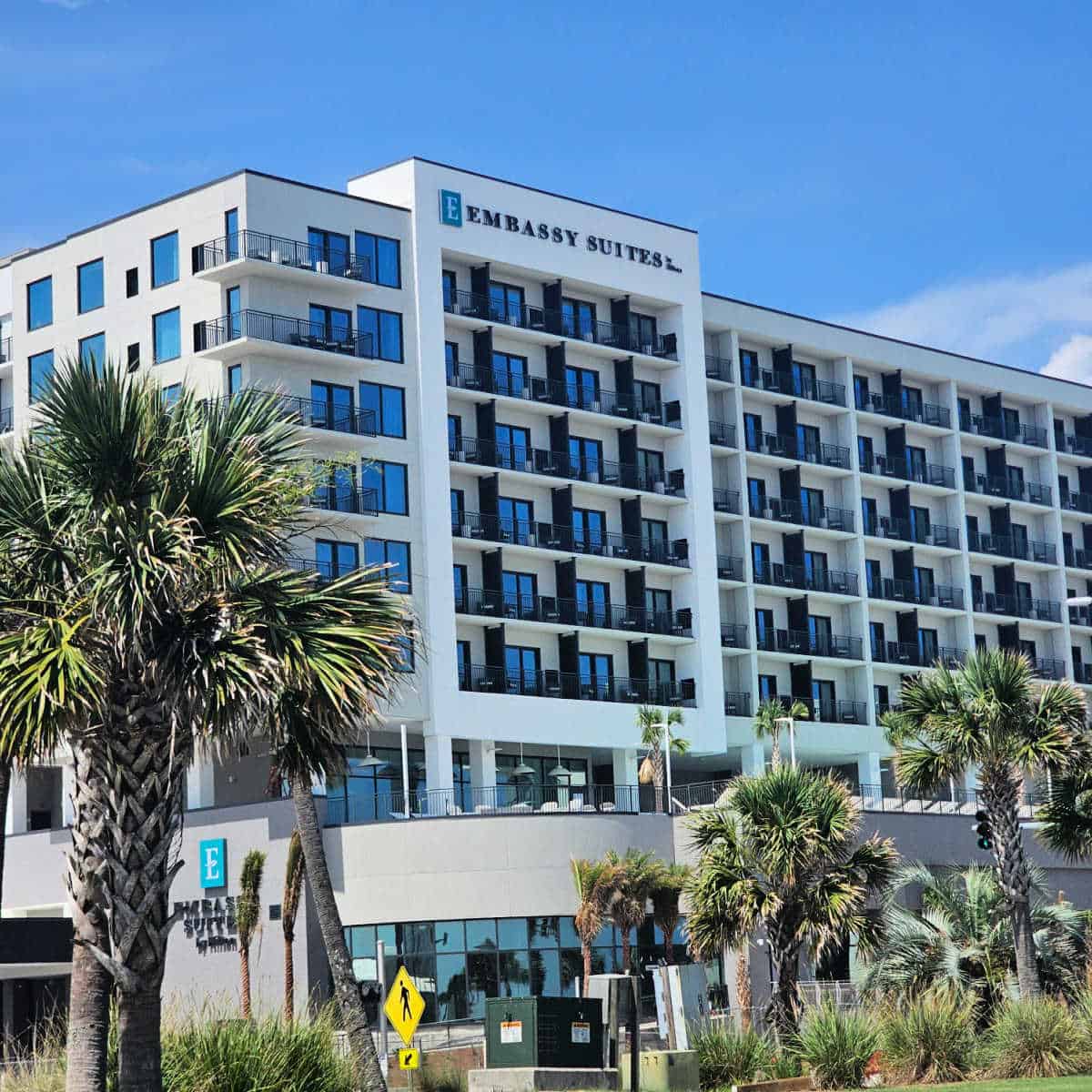 Embassy Suites by Hilton sign on the top of a white hotel building with palm trees in the foreground
